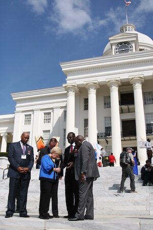 On March 25, 2015, following ceremonies marking the 50th anniversary of the Selma March ending at the Montgomery statehouse, Peggy Wallace Kennedy, daughter of Gov. George Wallace, who famously worked to preserve segregation, prays with leaders of The Reconciled Church. Left to right: Bishop Kyle Searcy of Fresh Anointing Church in Montgomery; Jim Liske, president of Prison Fellowship; Bishop Harry Jackson, The Reconciled Church founder (and senior pastor of Hope Christian Church near Washington, D.C.); and Bishop J. Alan Neal of the International Communion of Evangelical Churches.